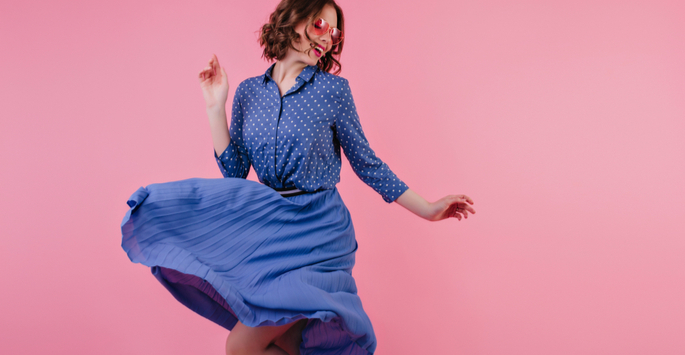Joyful, confident woman wearing a blue polka dot blouse and blue skirt dancing